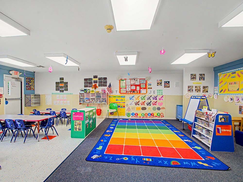 Colorful preschool classroom with tables, chairs, and a rainbow rug