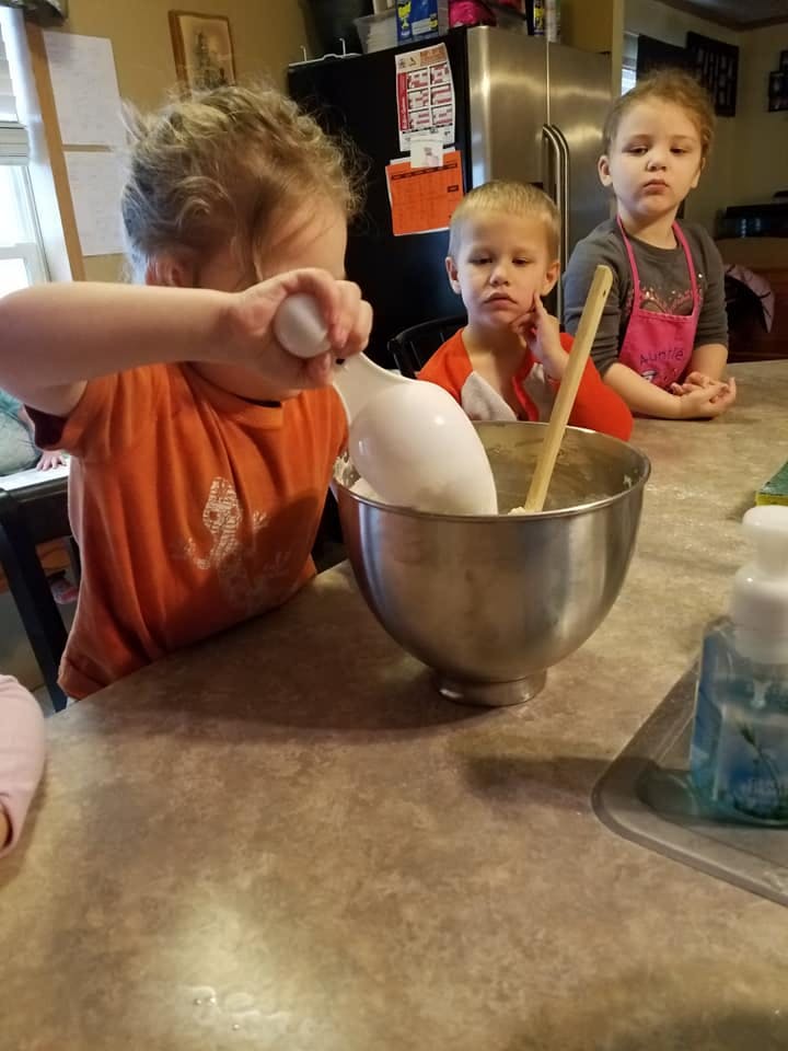 Child mixing ingredients in a bowl with two other children watching