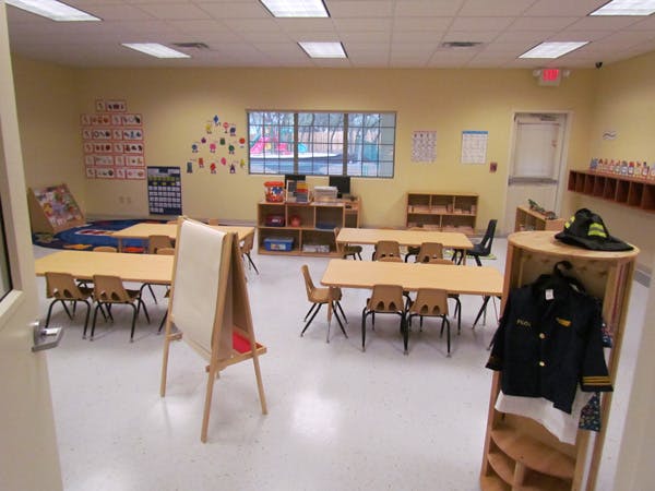 Empty classroom with small tables and chairs, an easel, and a dress-up station