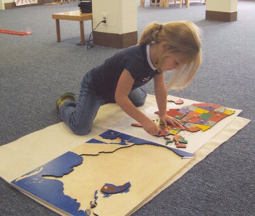 Child kneeling on floor assembling a map puzzle