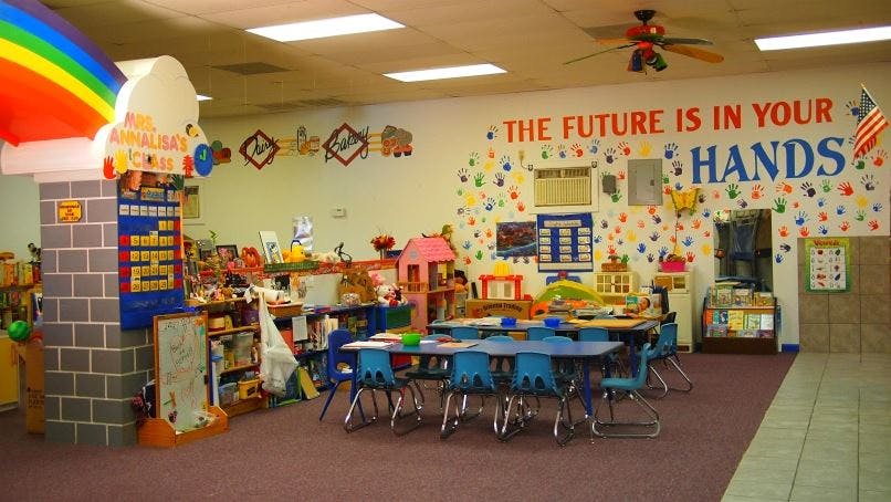Preschool classroom with small tables and chairs, and a wall mural