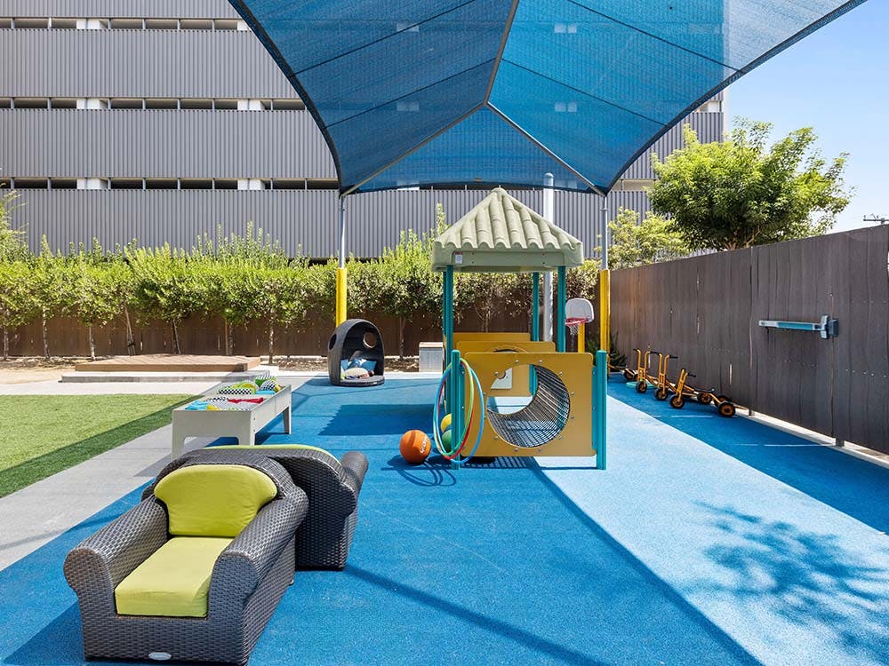 Outdoor children's play area with blue ground, play structure, and small bikes