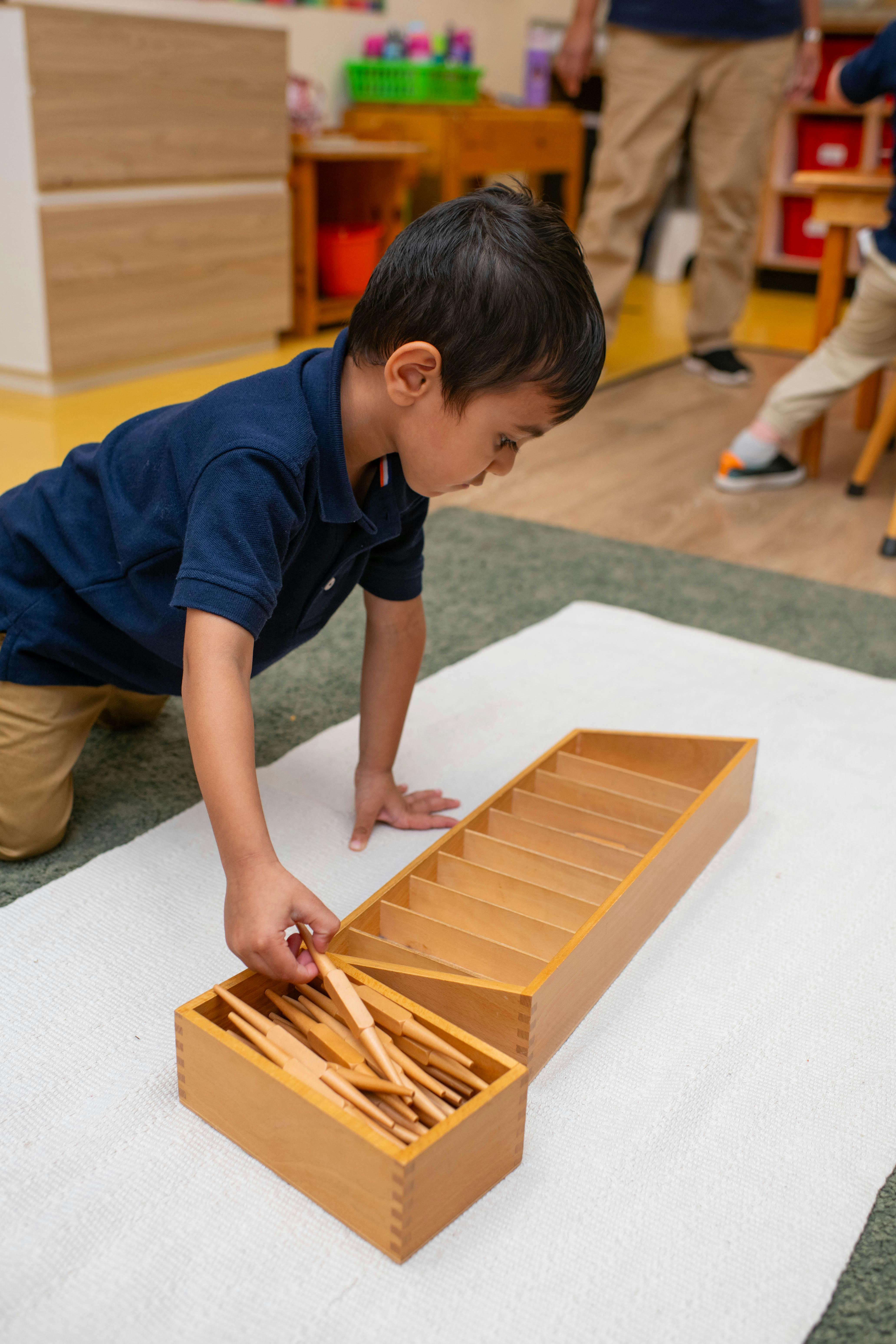 Child kneeling and playing with wooden blocks in a box on a mat