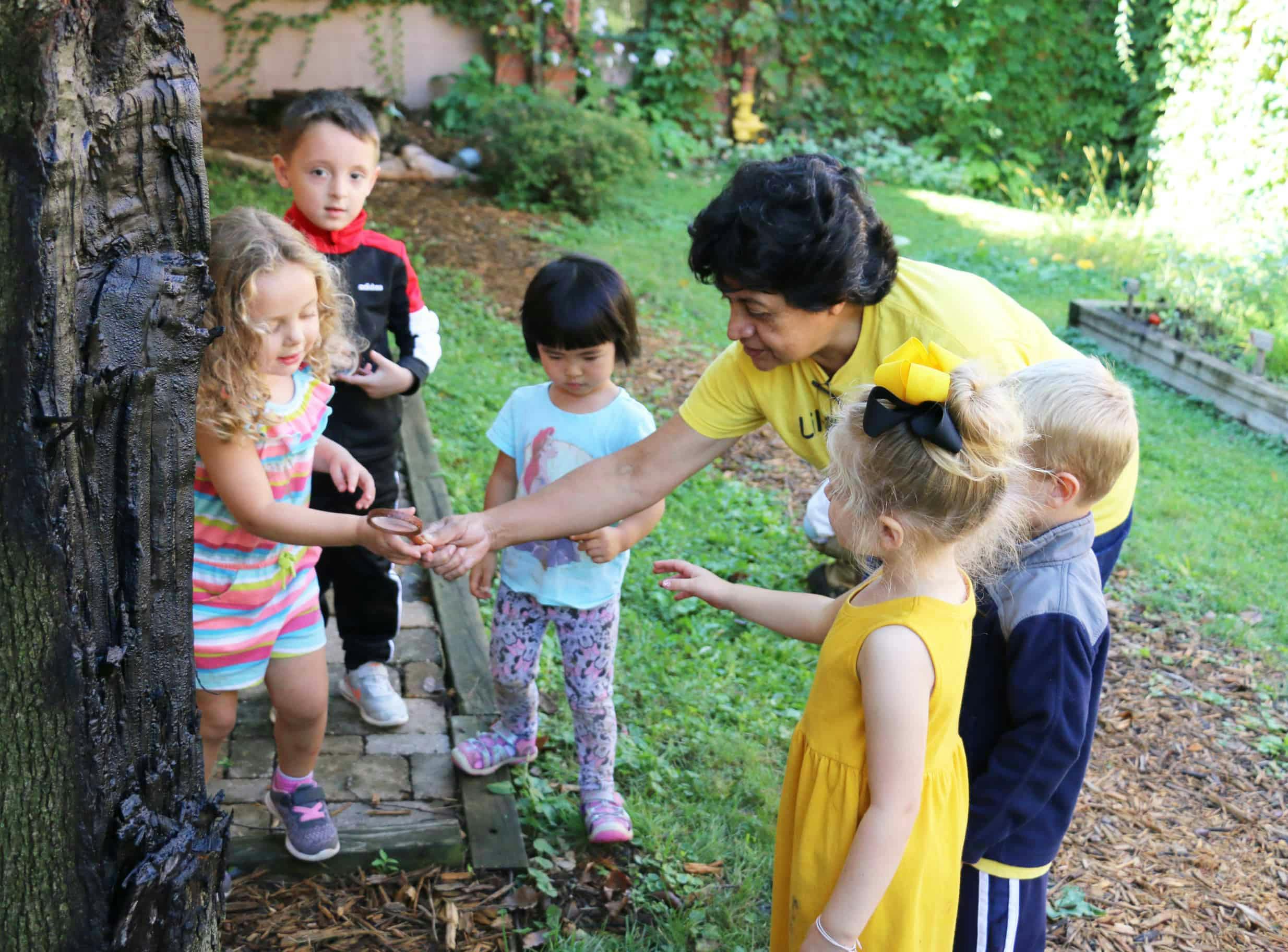 Adult and multiple children looking at something in a child's hand outdoors