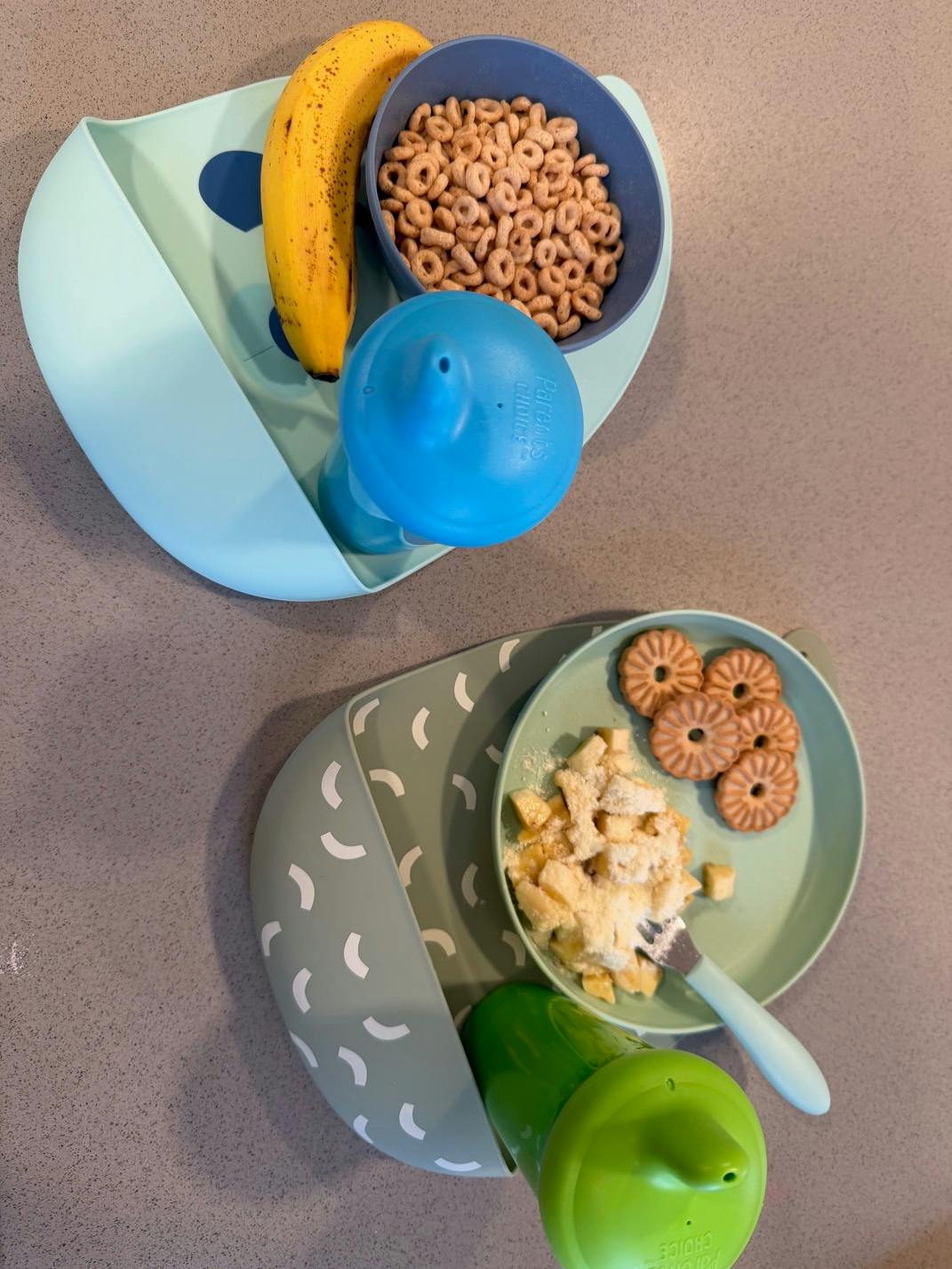 Two children's meals with bibs, one with cereal and banana, one with pasta and cookies