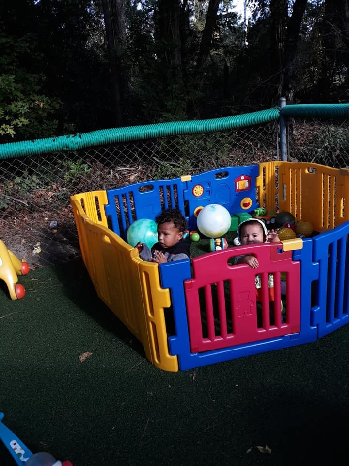 Two children playing in a colorful playpen outdoors
