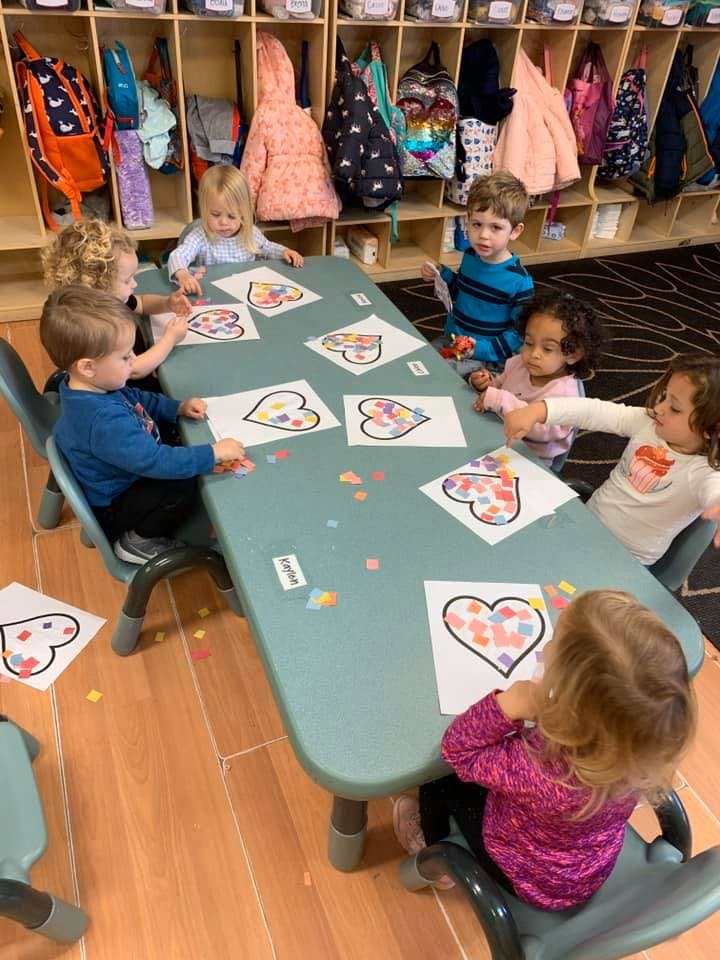 Children sitting at a table doing crafts with heart shapes