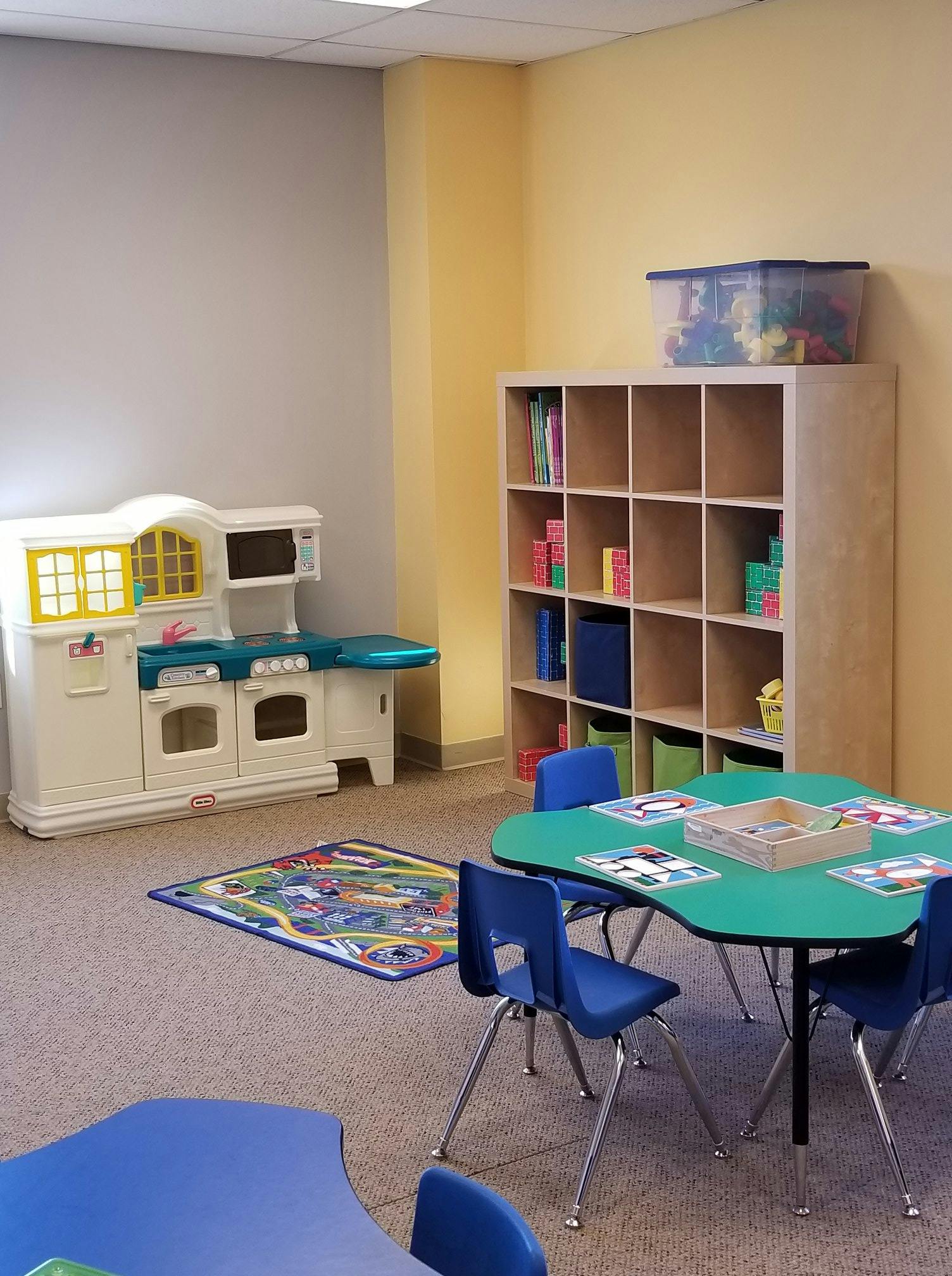 Play kitchen, cubby shelf, and small tables with chairs in a classroom