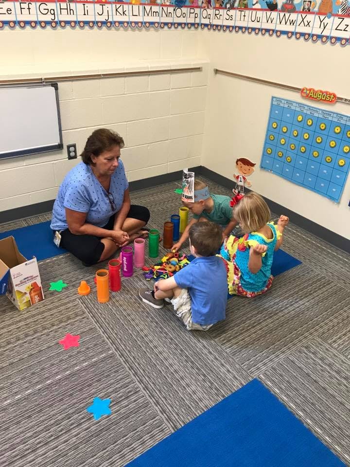 Adult and three children playing with colorful toys on the floor in a classroom