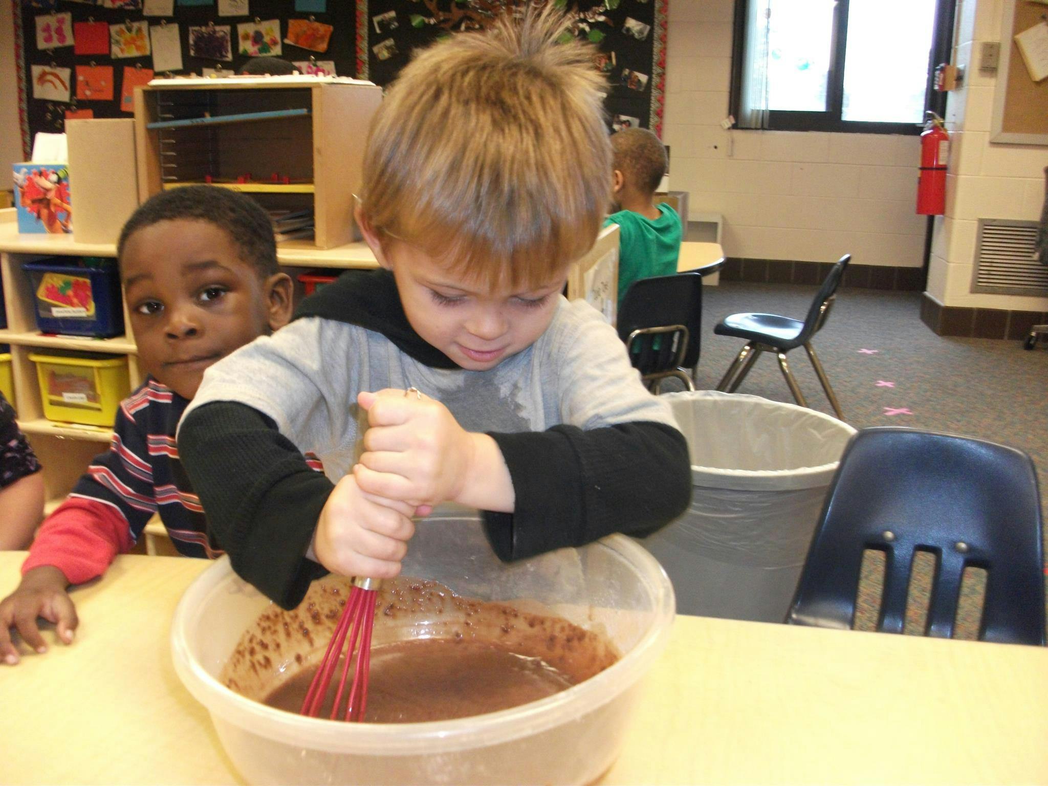 Child whisking mixture in a bowl in a classroom