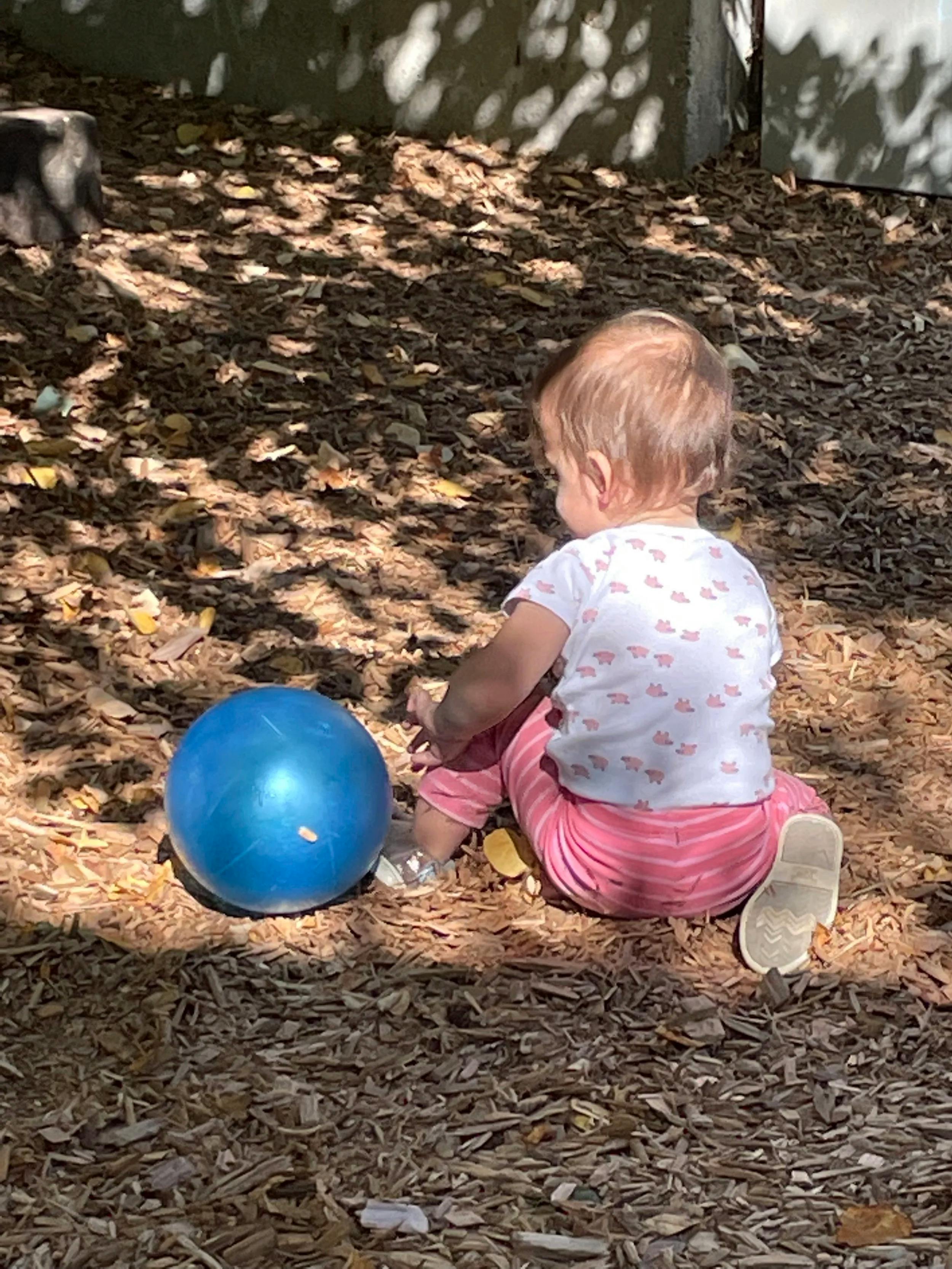 Child sitting on wood chips with a blue ball