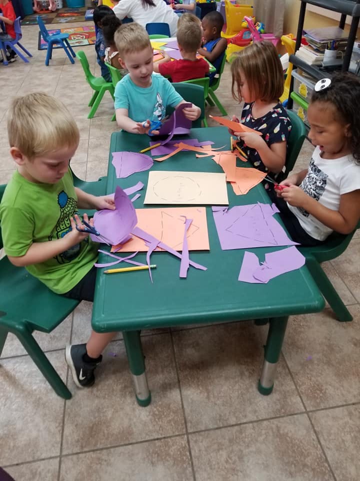 Children cutting paper at a table in a classroom