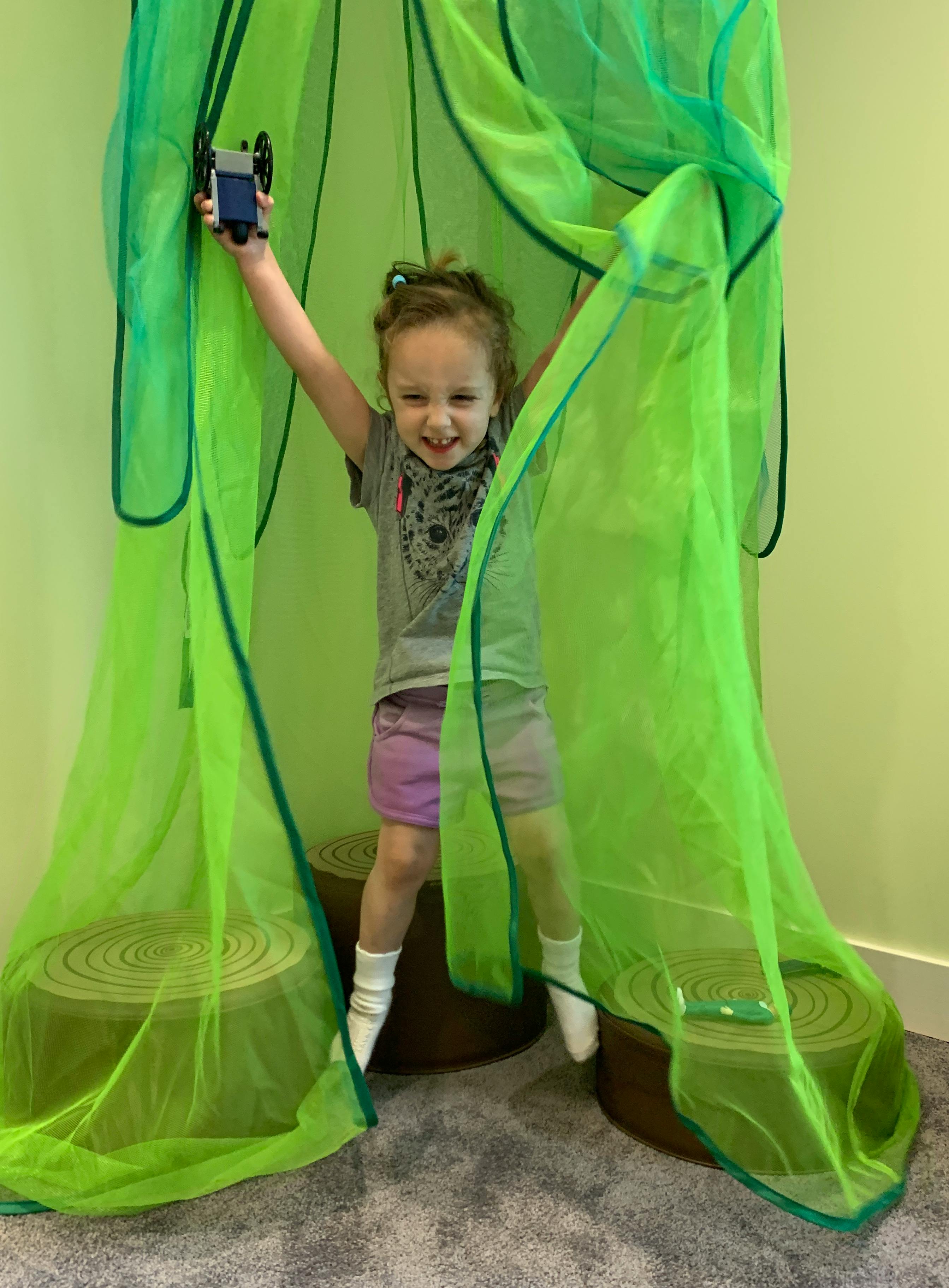 Child standing in green netting, holding a toy above head