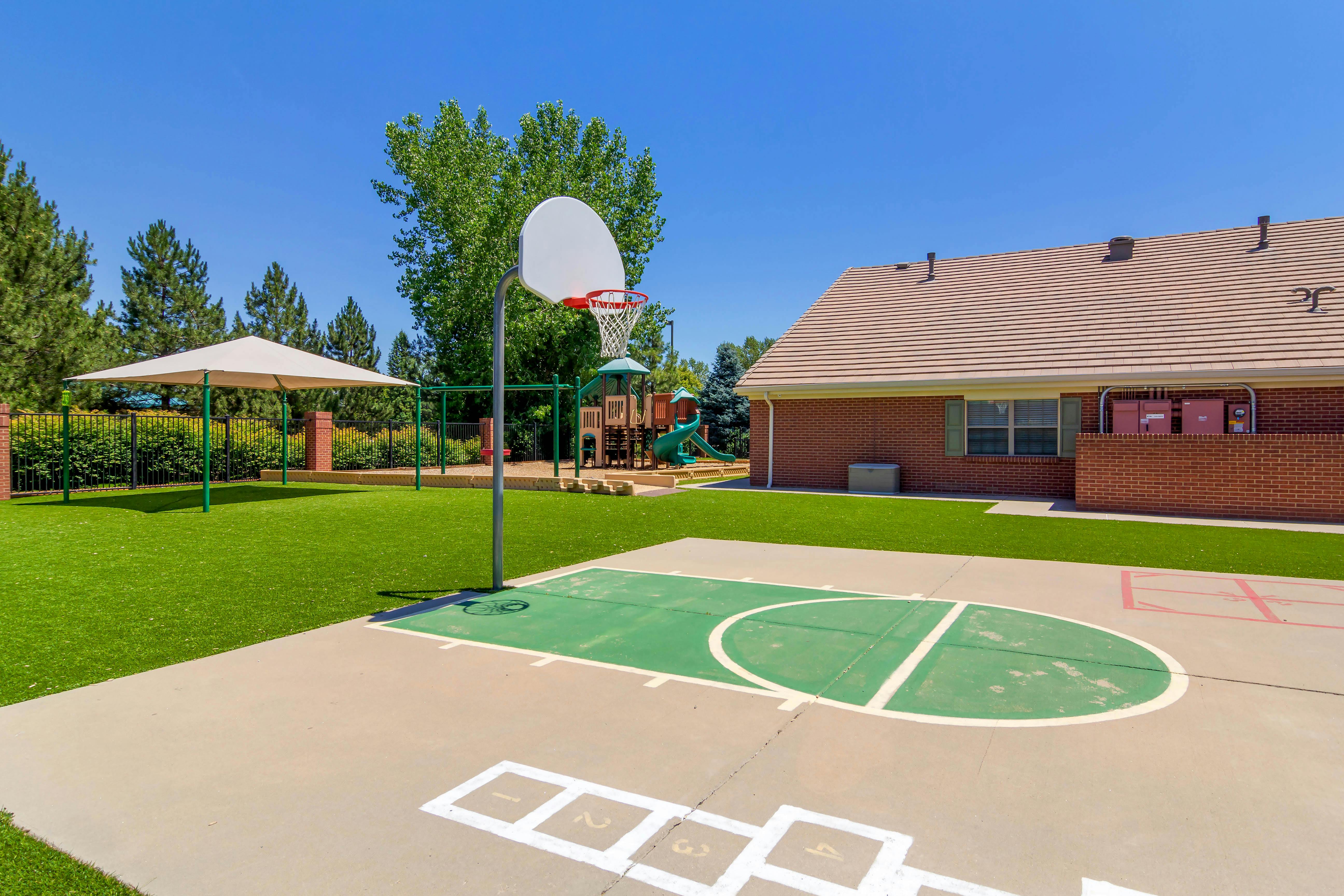 Basketball hoop on a court with hopscotch squares and a playground with artificial turf