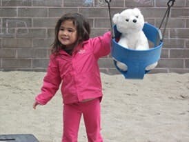 Child standing next to a swing with a white stuffed animal