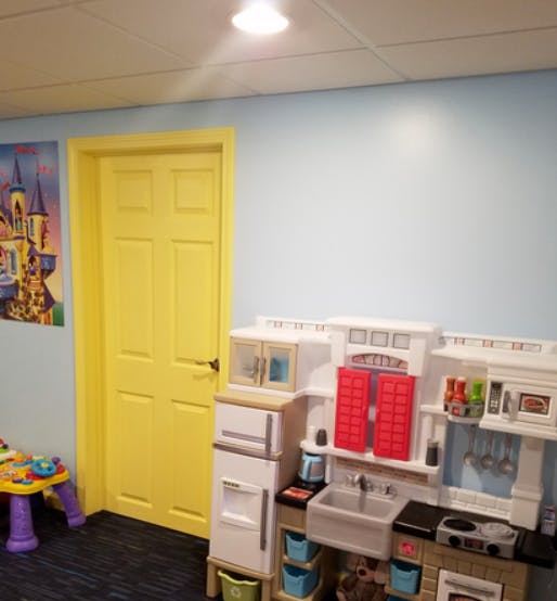Yellow door next to a toy kitchen set and a small table