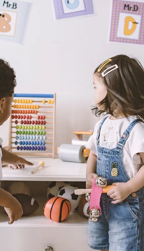 Two children playing with an abacus and toys in a classroom