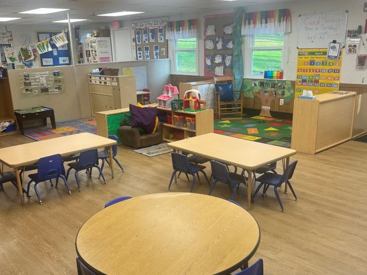 A classroom with small tables and chairs, toys, and a calendar on the wall