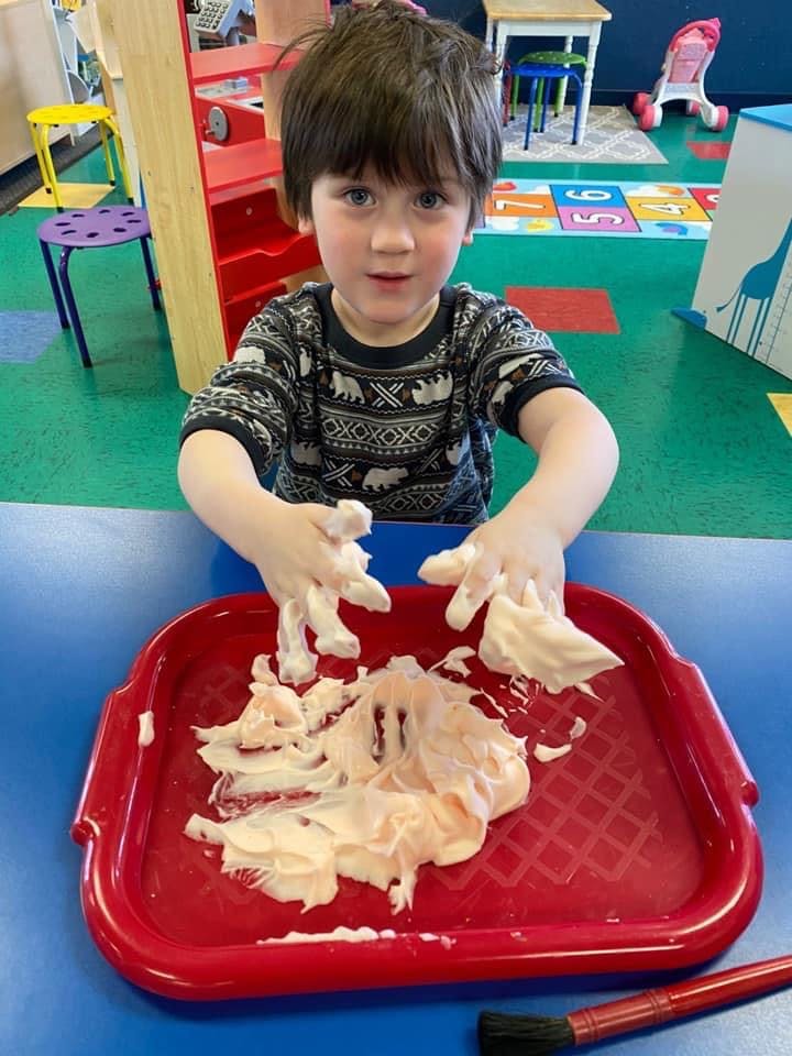 Child playing with shaving cream in a red tray