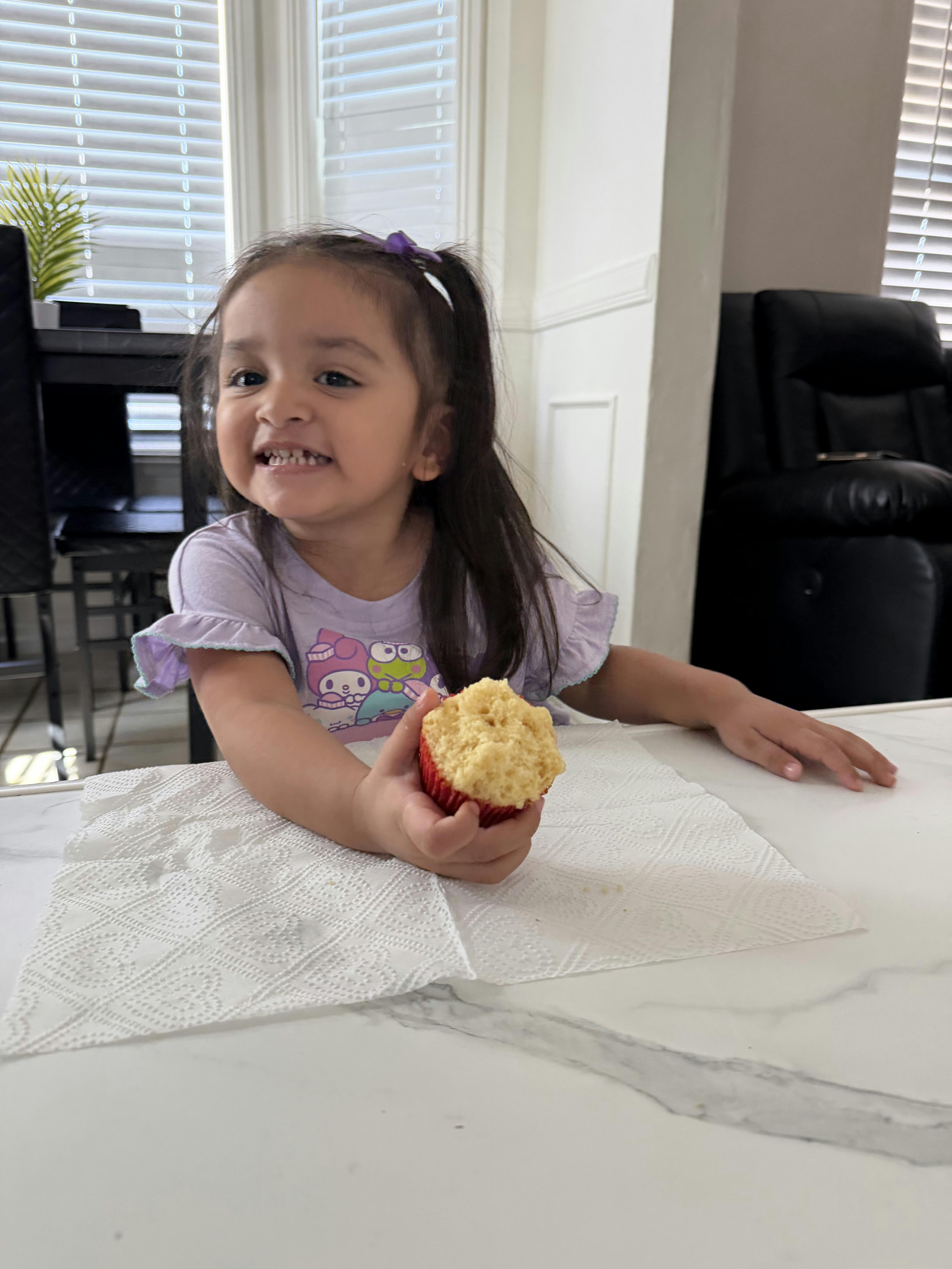 A smiling child holding a cupcake at a table