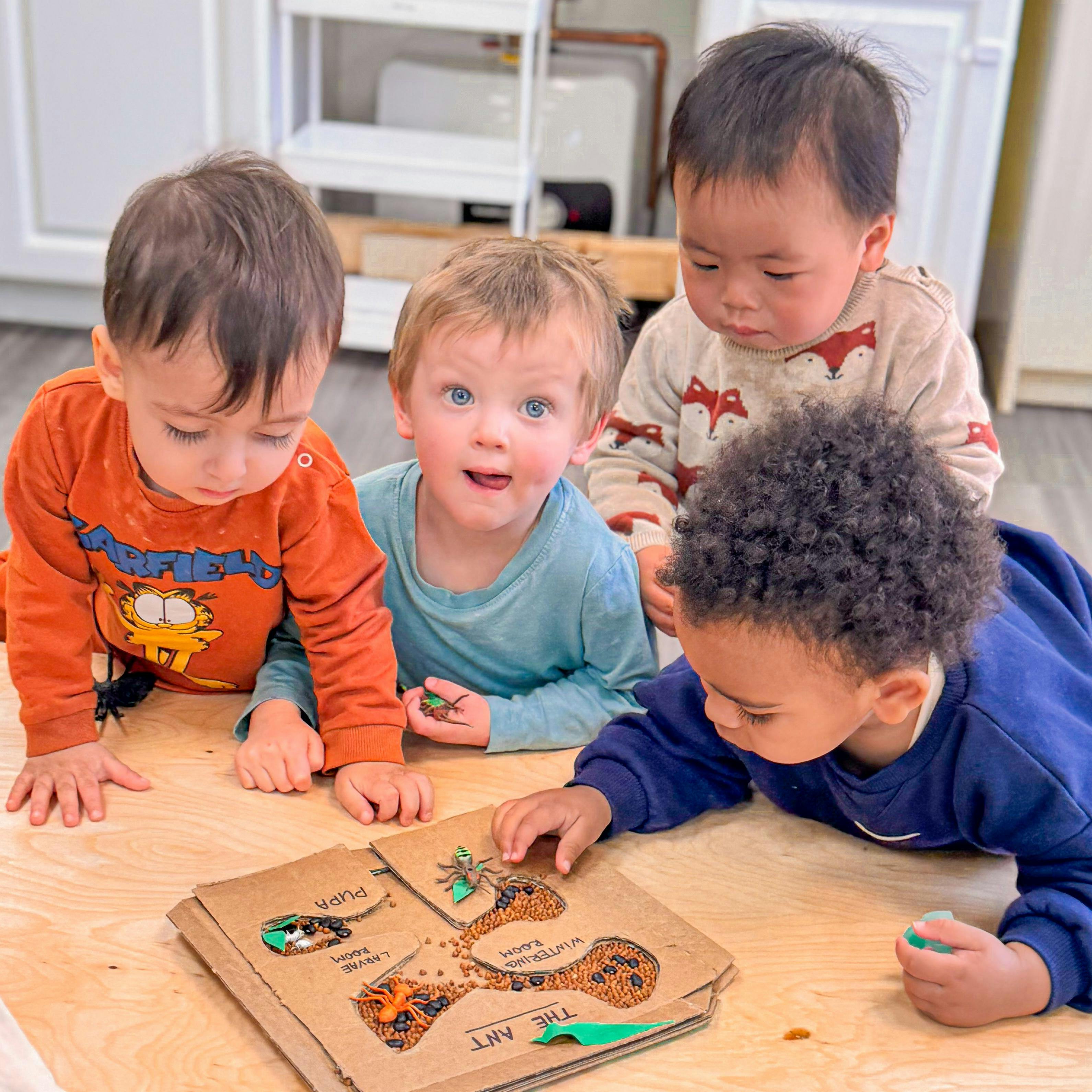 Four children interacting with an ant lifecycle activity board on a table
