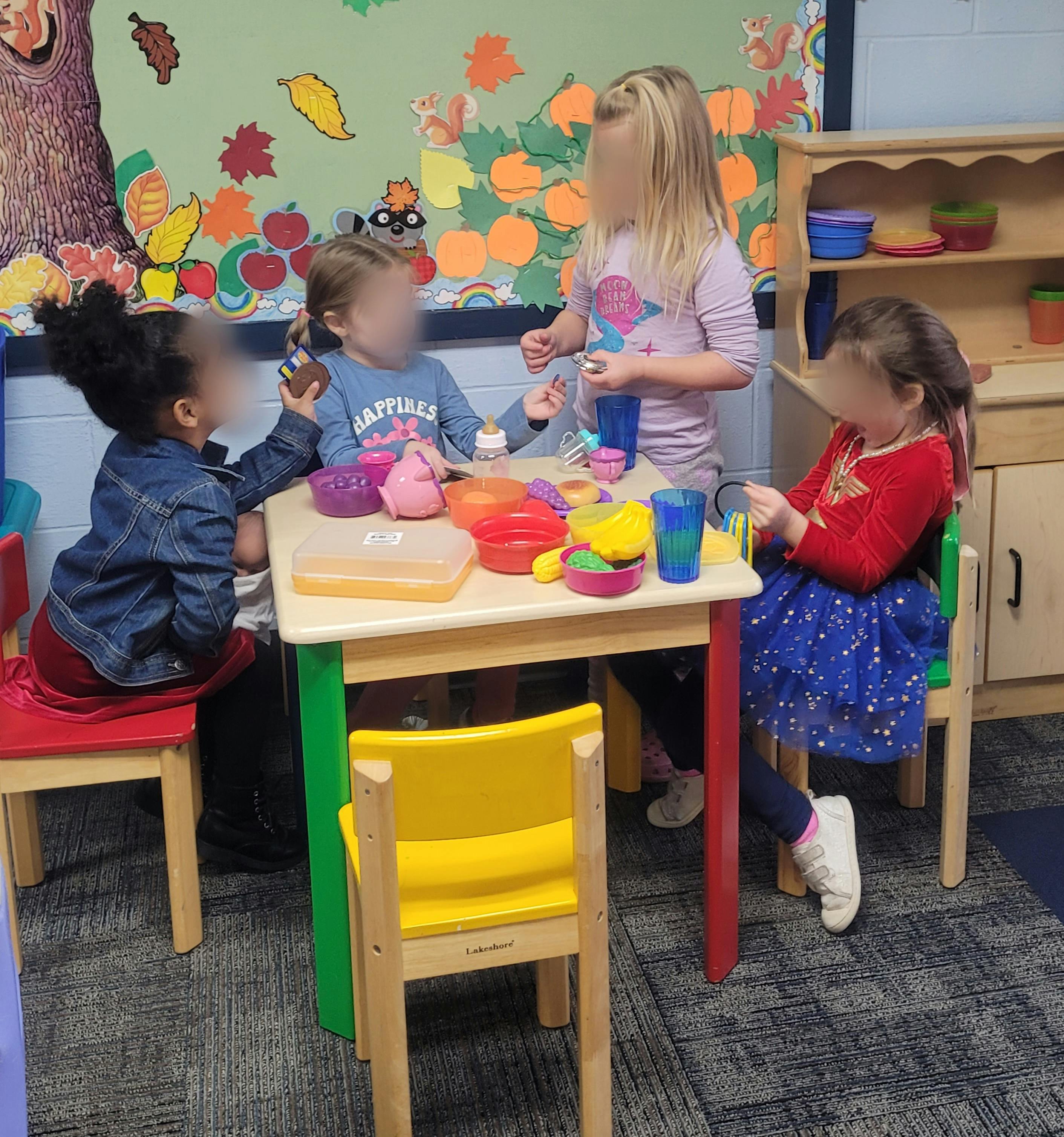 Four children playing with colorful dishes at a small table in a classroom