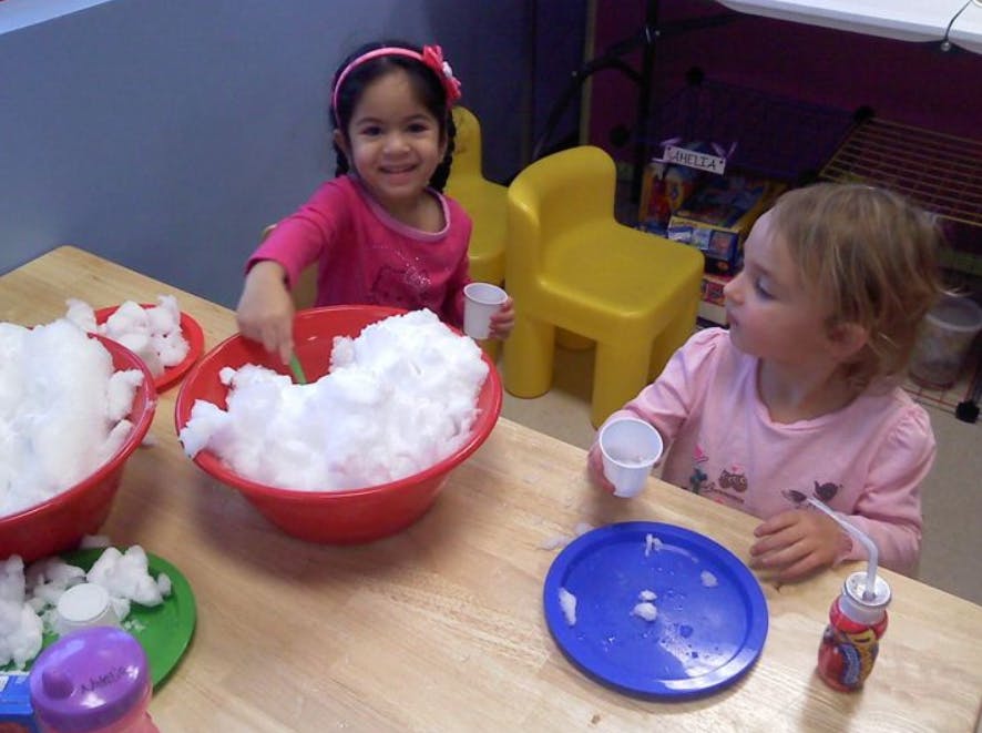 Two children playing with bowls of white fluffy material at a table