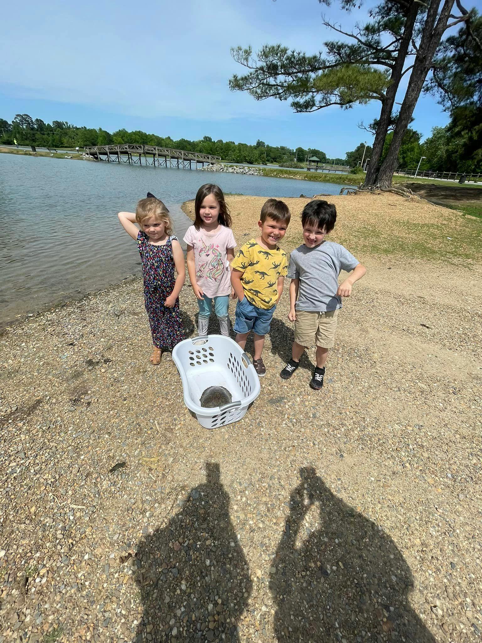 Four children standing on a shore next to a basket with a turtle