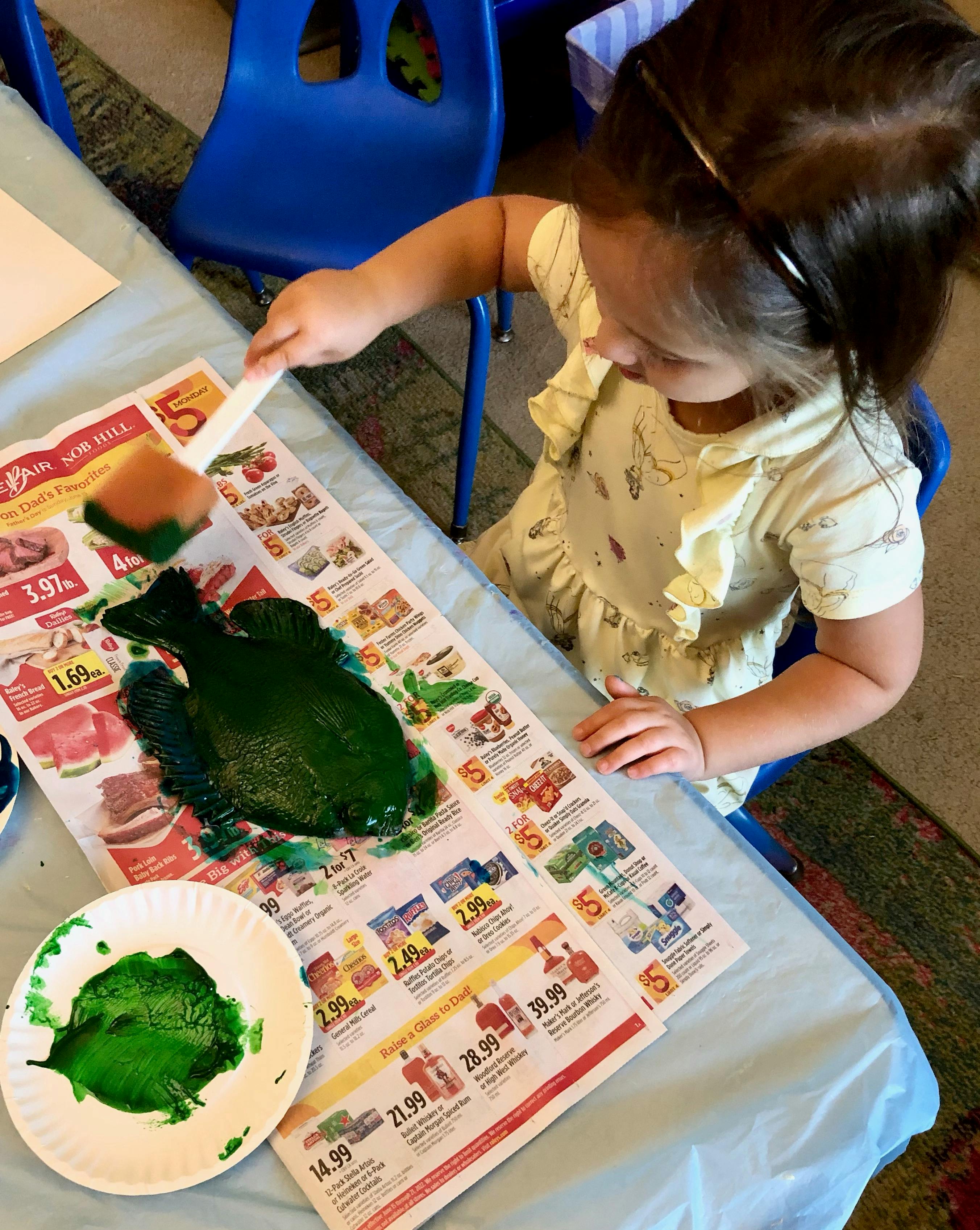Child painting a green shape on newspaper