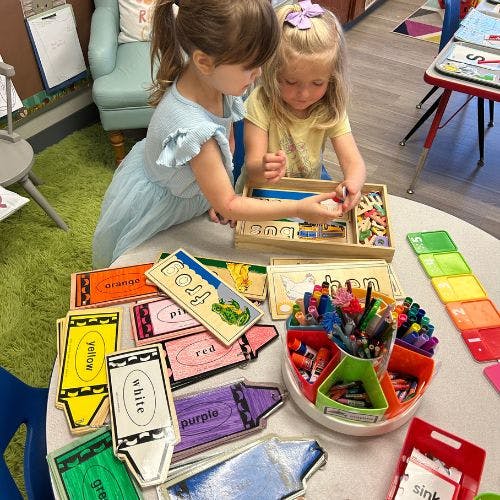 Two children playing with learning toys and crayons at a table
