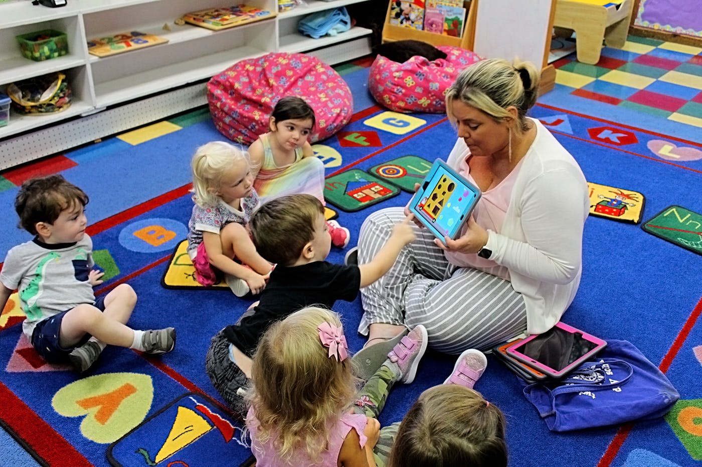 Adult and children sitting on a colorful rug looking at a tablet