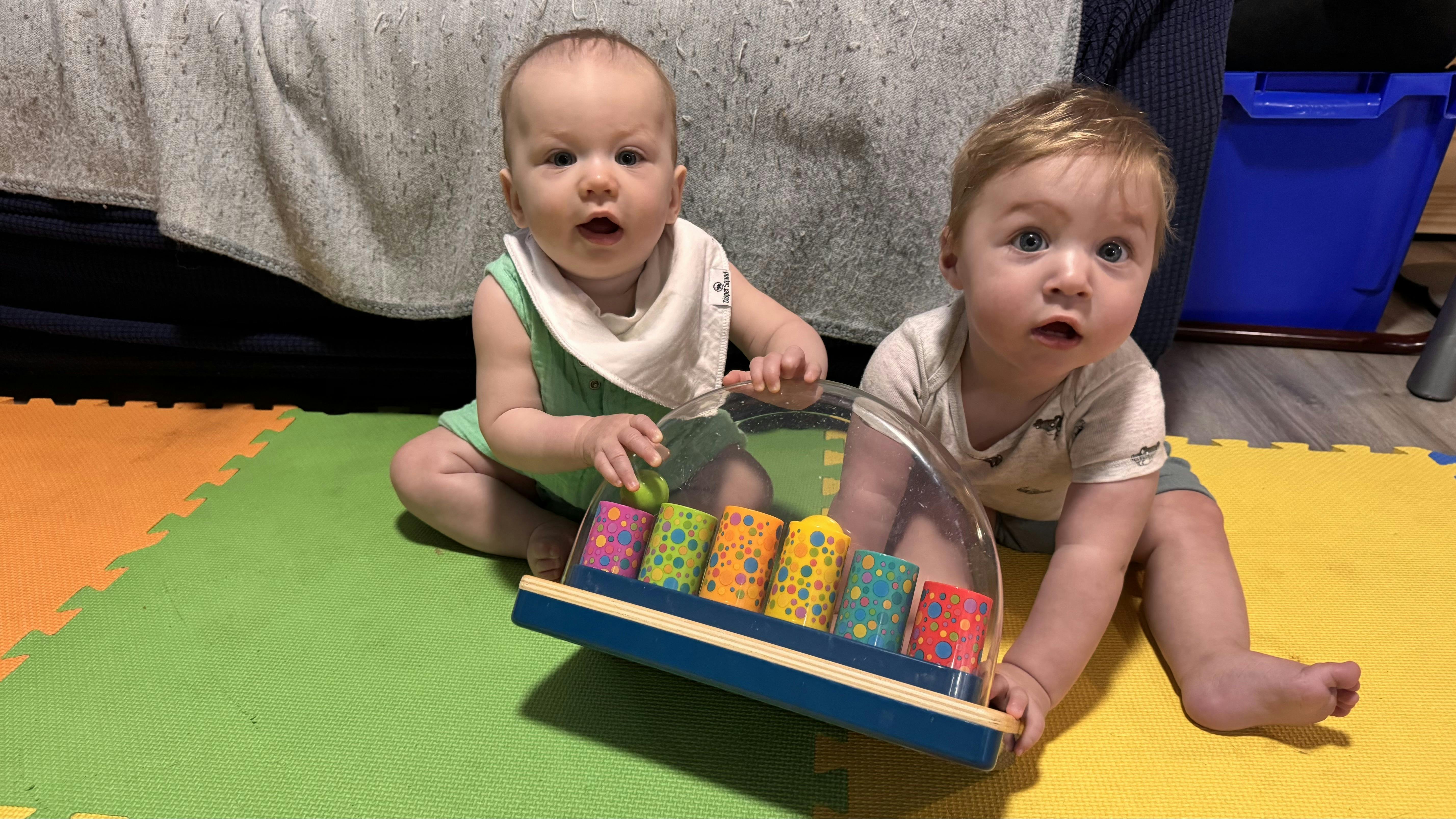 Two children sitting on a playmat with a toy