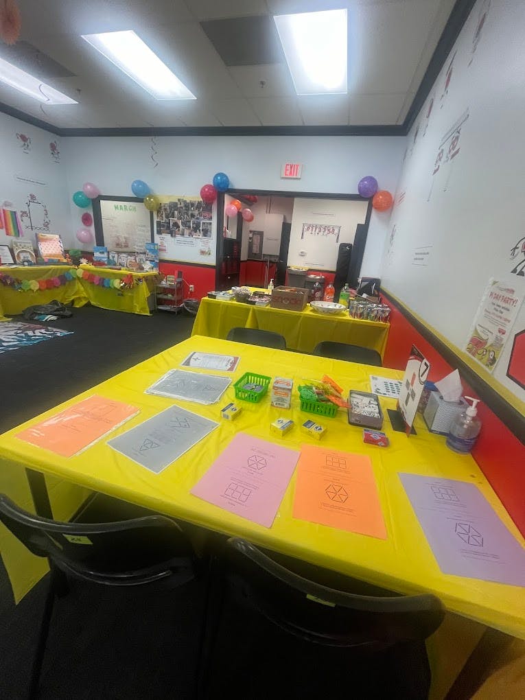 Room with yellow-covered tables displaying various items and balloons