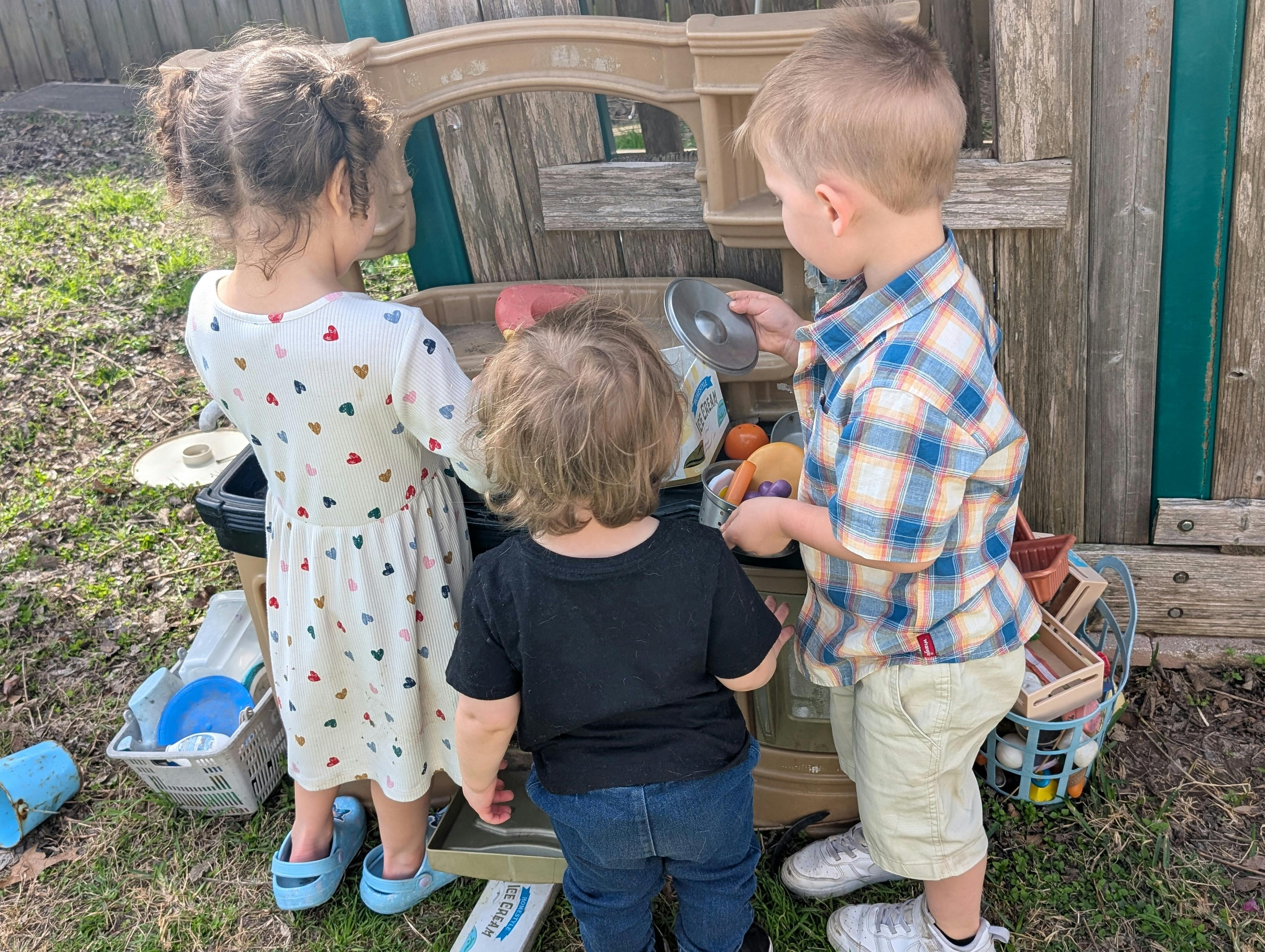 Three children playing outdoors with a toy kitchen set