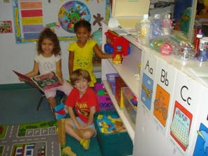 Three children in a classroom, one reading a book