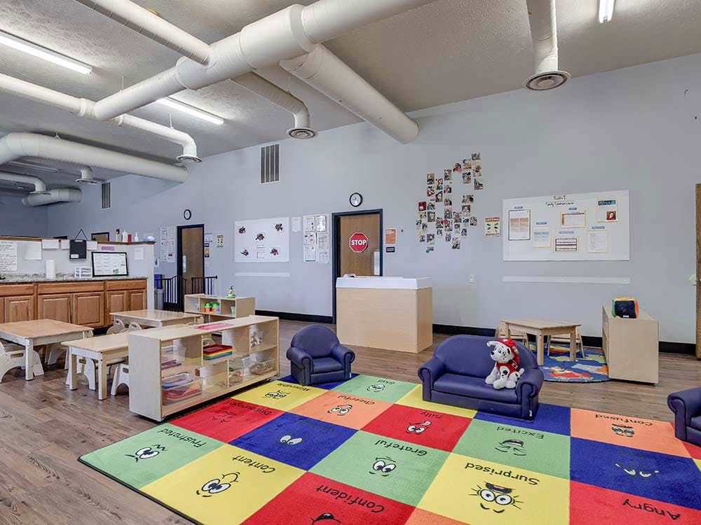 Children's classroom with small tables, chairs, colorful rug, and exposed ceiling ducts