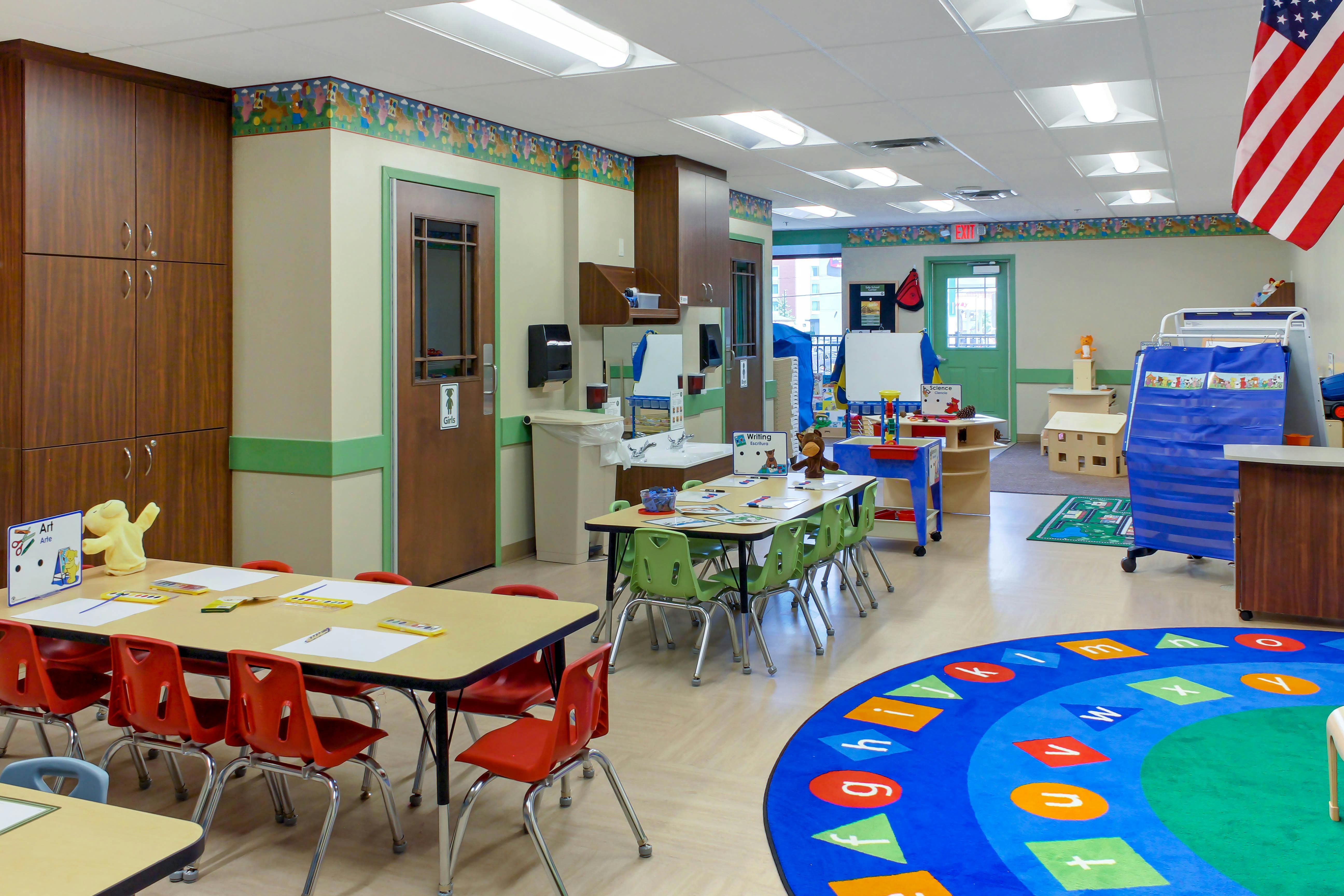 Classroom with child-sized tables and chairs, alphabet rug, and an American flag