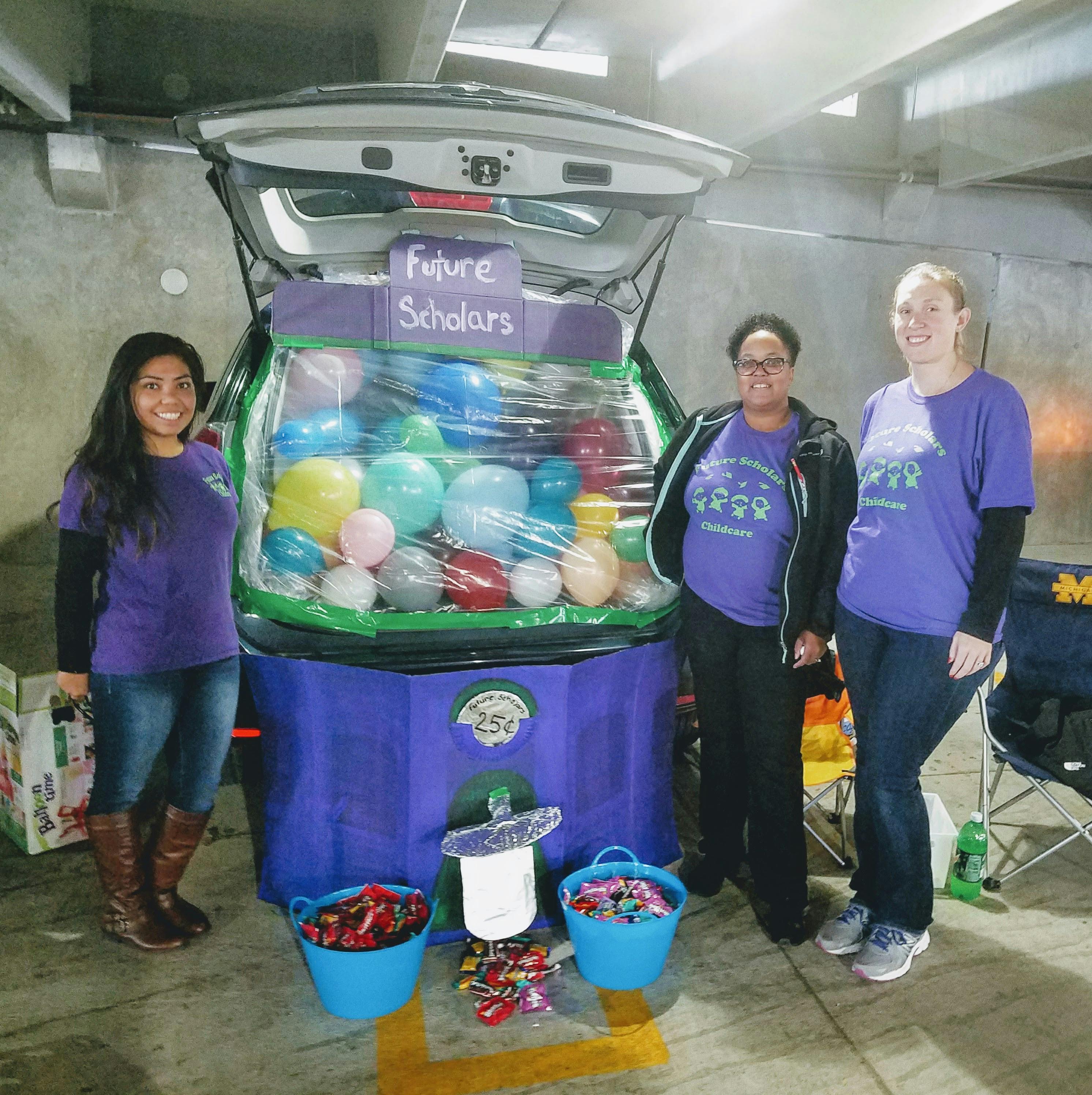 Three people standing next to a car trunk decorated with balloons and candy