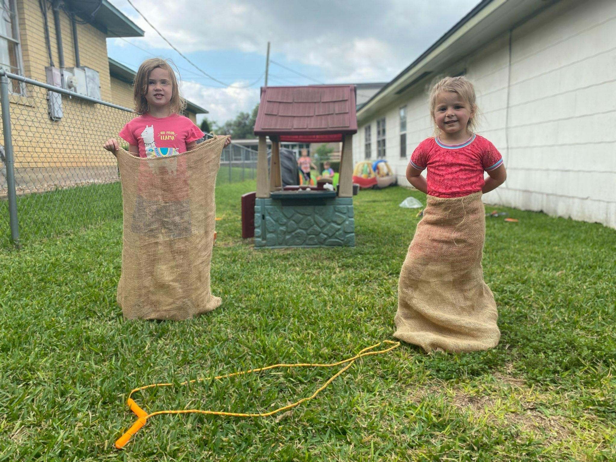 Two children in burlap sacks standing on grass