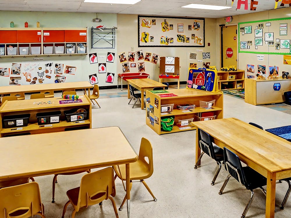 Empty classroom with small tables, chairs, and shelves with educational materials