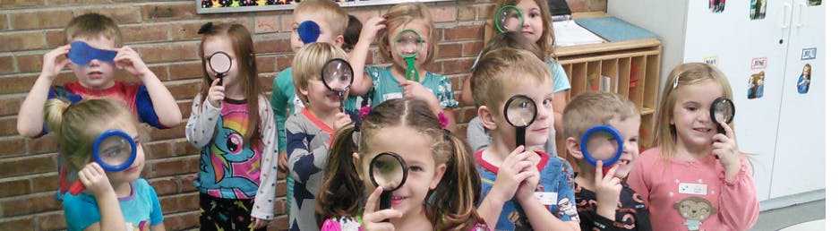 Children holding magnifying glasses to their eyes in a classroom