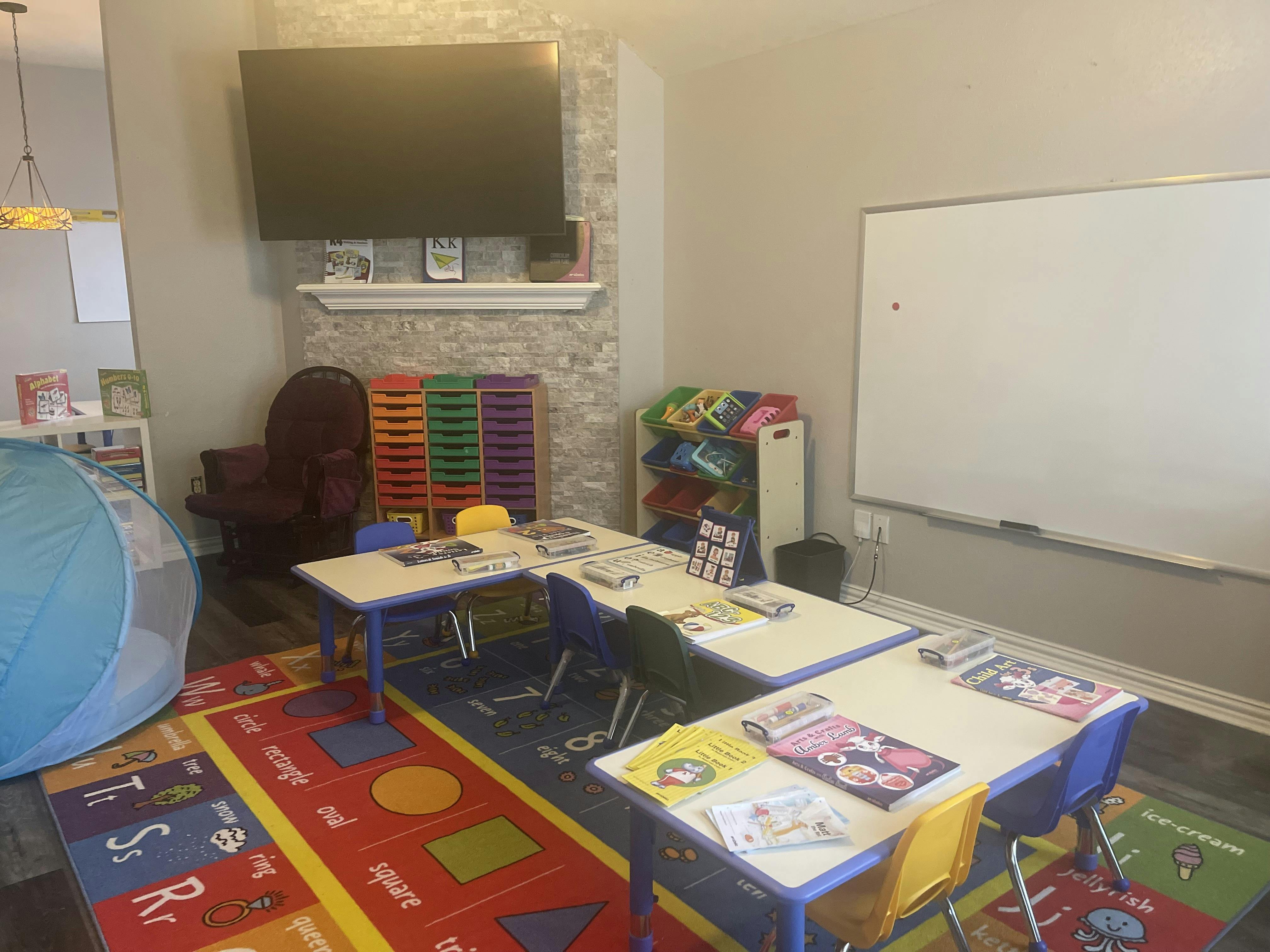 Classroom with small tables and chairs, a whiteboard, and a colorful rug