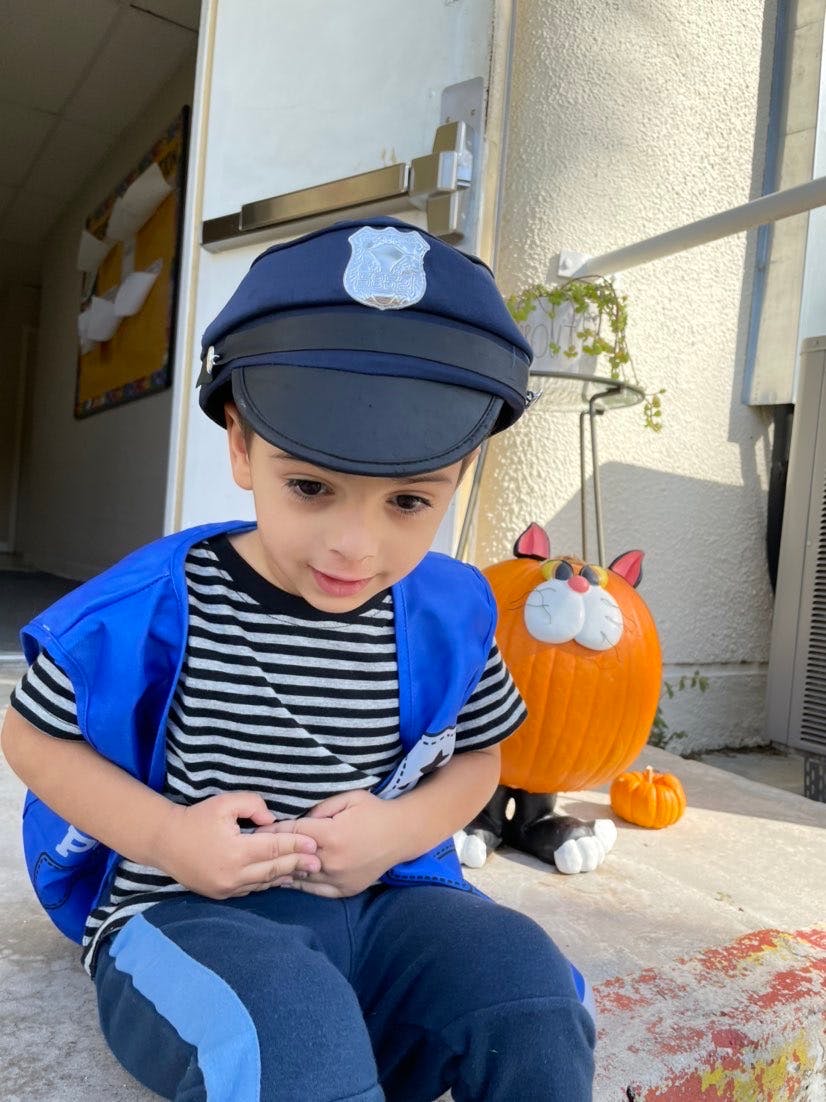 Child in a police hat and blue vest sitting next to a pumpkin decoration