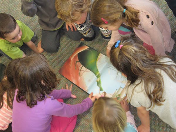Children gathered around a large open book on the floor