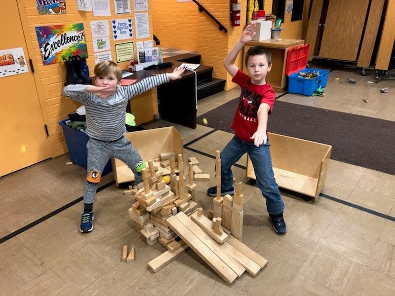 Two children posing next to a structure made of wooden blocks