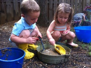 Two children playing in mud with shovels and buckets