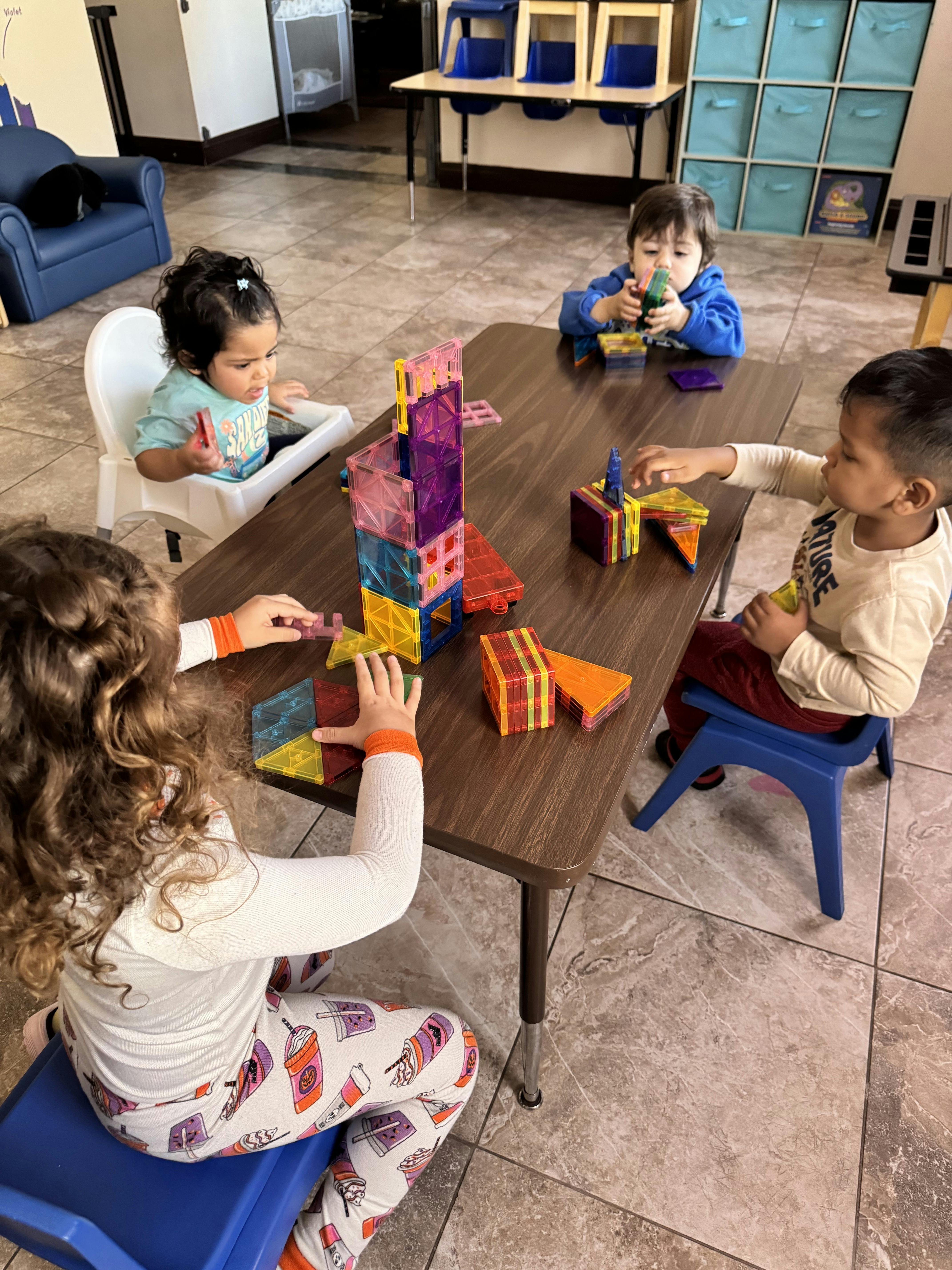 Four children sitting at a table playing with colorful magnetic building tiles