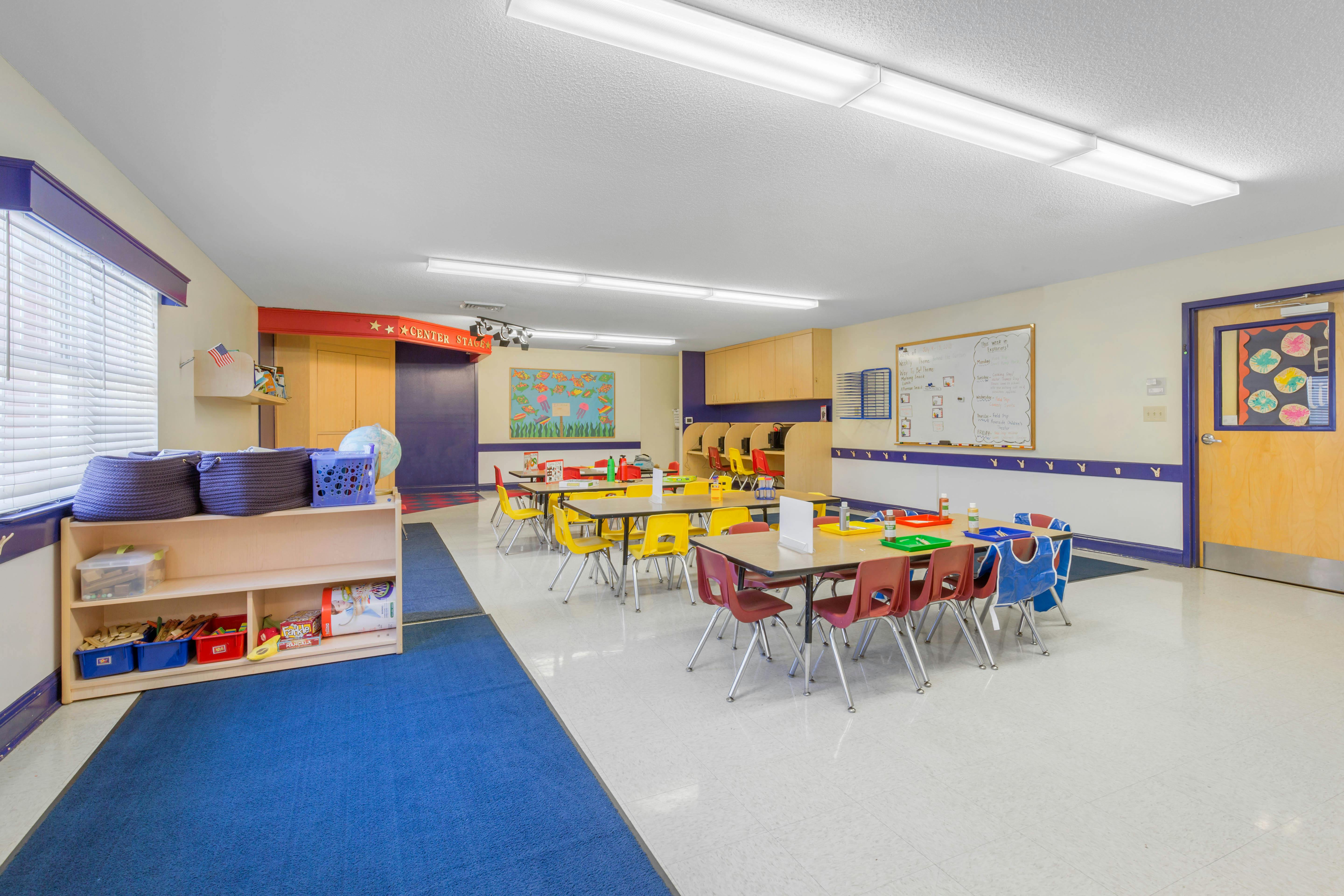 Classroom with small tables and chairs, shelves, and a whiteboard