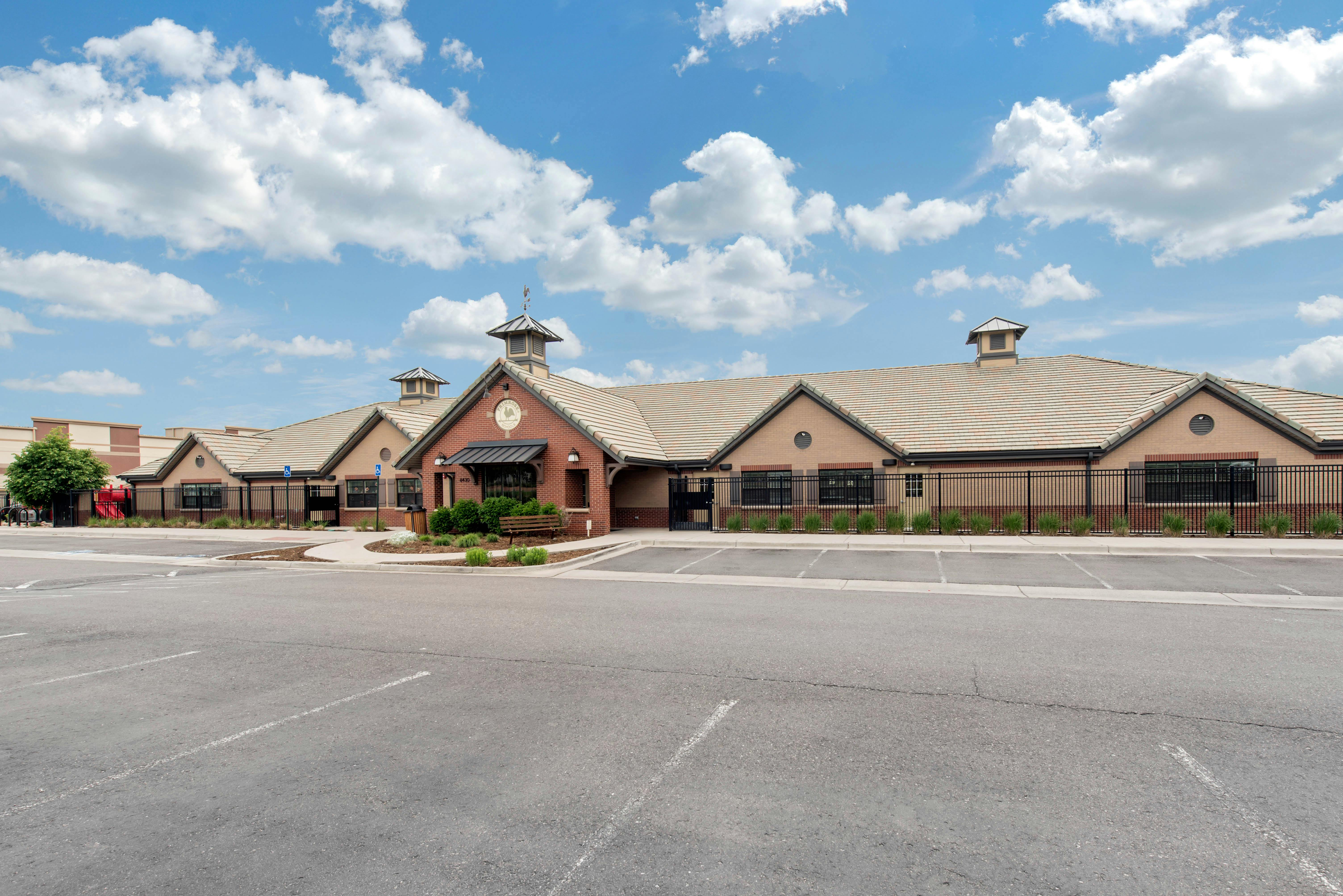 Building with brick and stucco siding and tile roof, parking lot in foreground