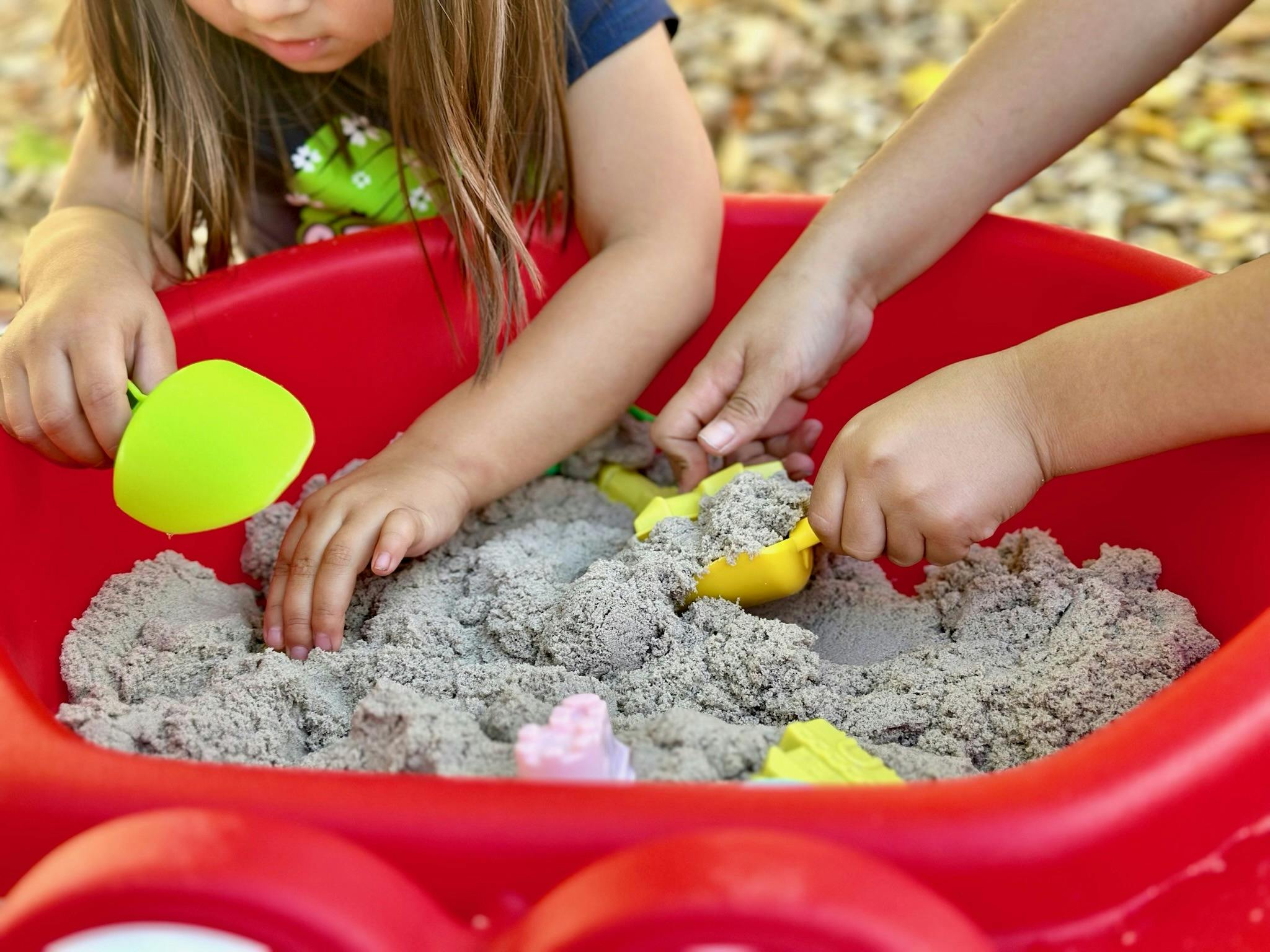 People playing with sand in a red basin using plastic scoops